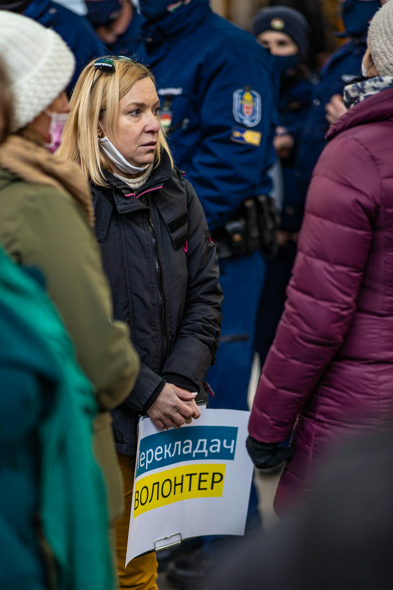 A volunteer stands amidst a crowd holding a sign during a Budapest event, showcasing community support.