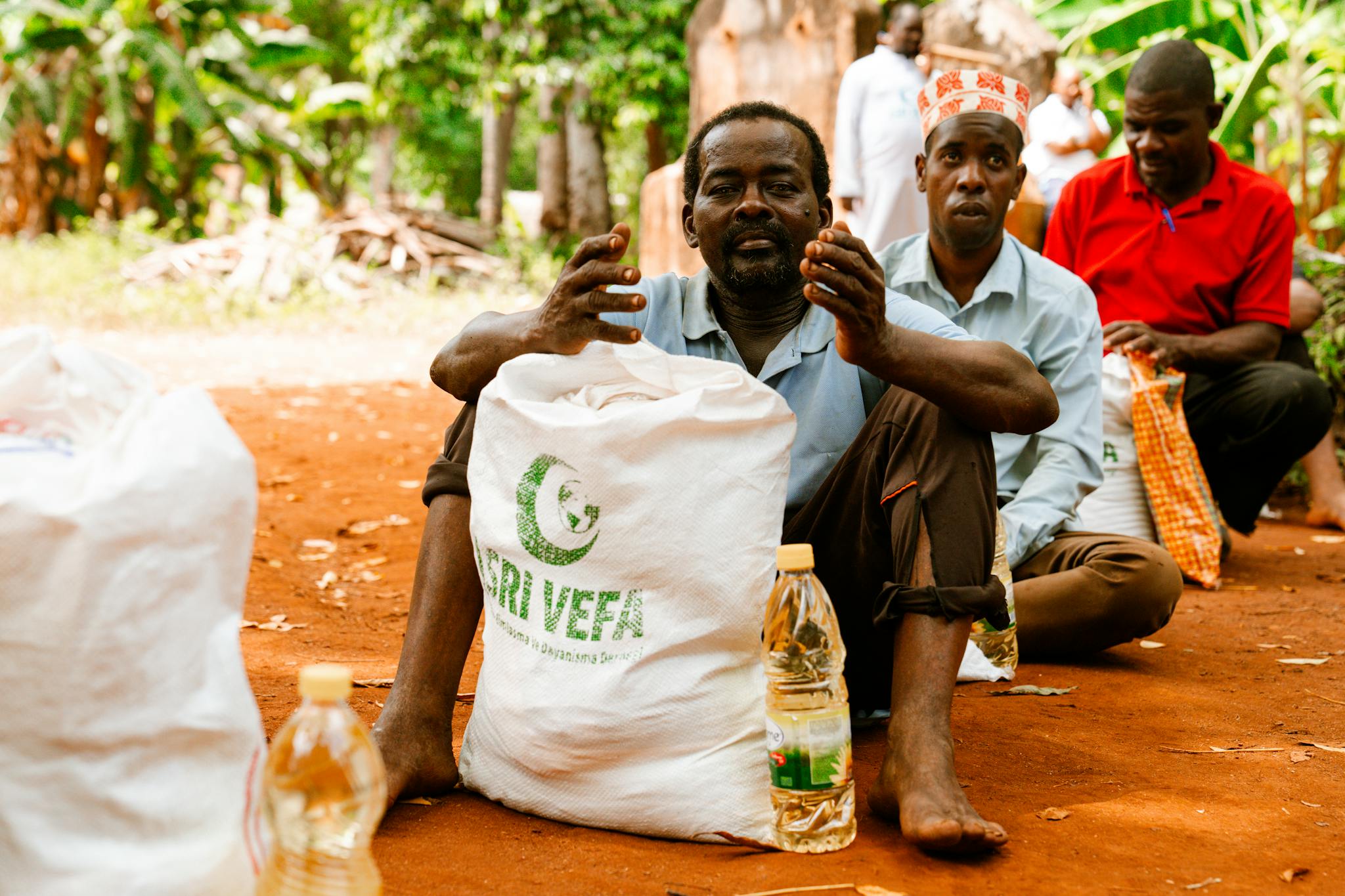 People seated outdoors with bags of supplies, indicating a community gathering.