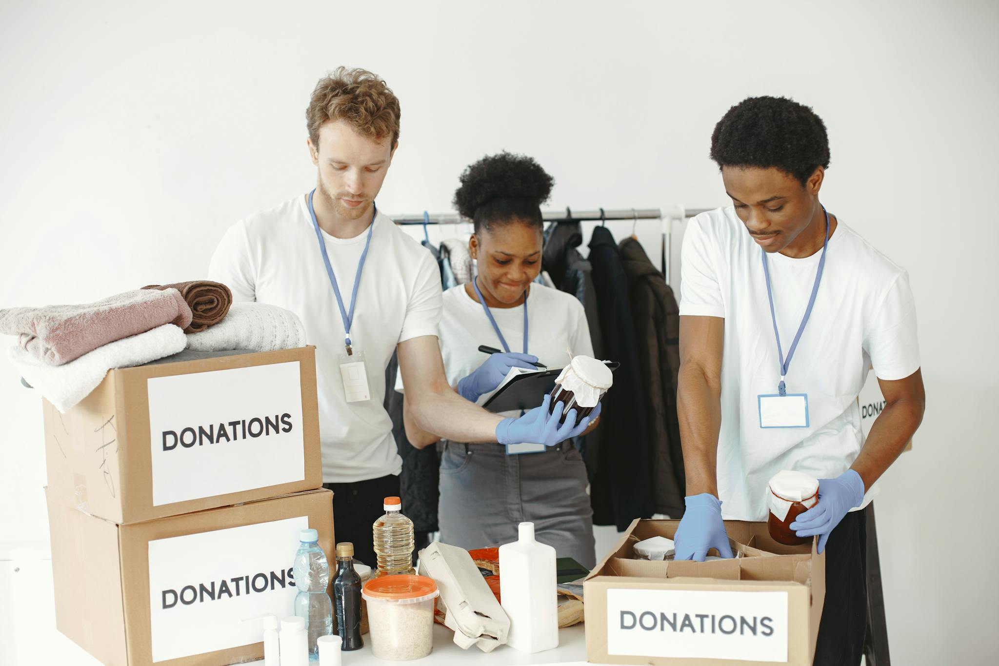 Three volunteers organizing donation boxes with clothes and food items in a community center.